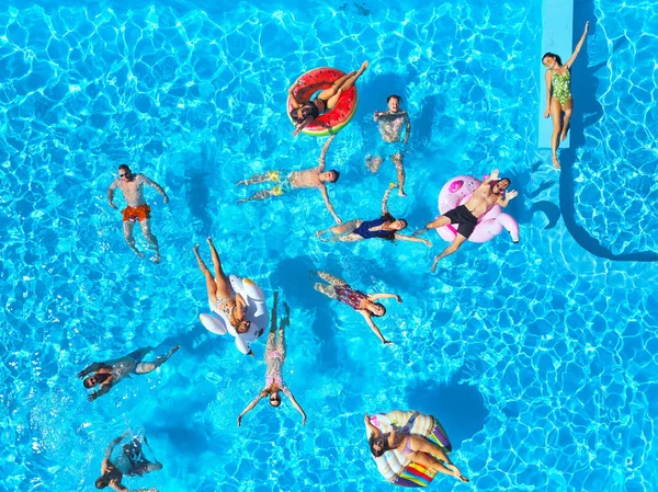 Aérea de amigos teniendo fiesta en piscina con flamenco inflable, cisne, colchón. Los jóvenes felices saludan con las manos a la cámara de drones en un resort de lujo. Vista desde arriba. Chicas en bikini tomando el sol. —  Fotos de Stock