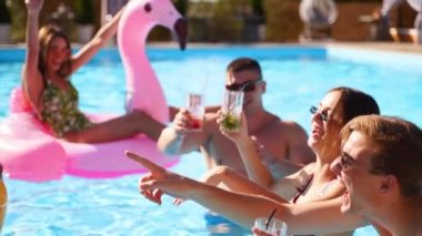 Arkadaşların havuzda kokteyllerle parti veriyor. Mayo dansındaki mutlu gençler, güneşli bir günde şişme flamingo, kuğu ve şilte ile gece kulübü. Yavaş çekim