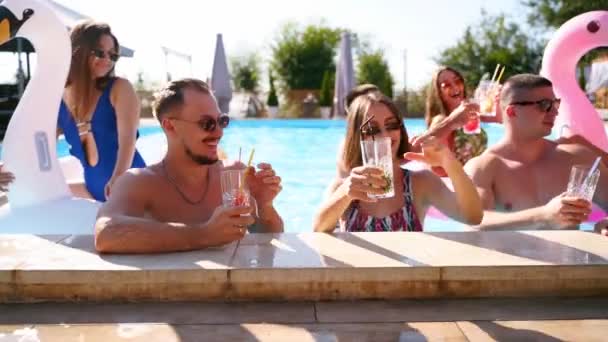 Amigos teniendo fiesta con cócteles en la piscina villa de vacaciones. Jóvenes felices en traje de baño bailando, bailando con flamenco inflable, cisne, colchón en un resort de lujo en un día soleado. Movimiento lento — Vídeo de stock