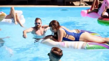 Arkadaşlar özel bir villada yüzüyorlar, şişme flamingo, kuğu ve şamandıralarda güneşe yatıyorlar. Gençler güneşli bir günde lüks bir tatil köyündeki partide rahatlar. Bikinili kızlar güneşleniyor. Süzül.