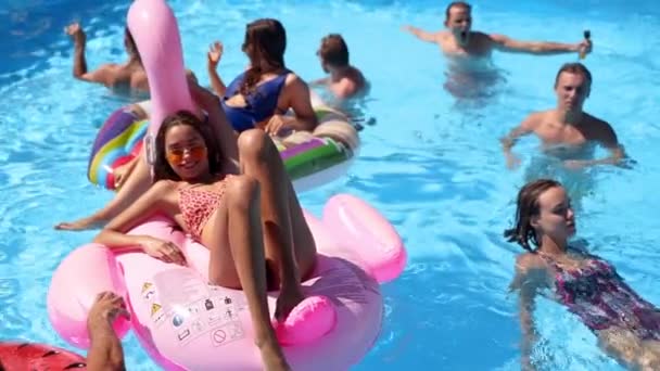 Friends chilling in private villa swimming pool, lie in the sun on inflatable flamingo, swan, floaties. Young people relax on party at luxury resort on sunny day. Bikini girls sunbathing. Slow motion. — Stock Video