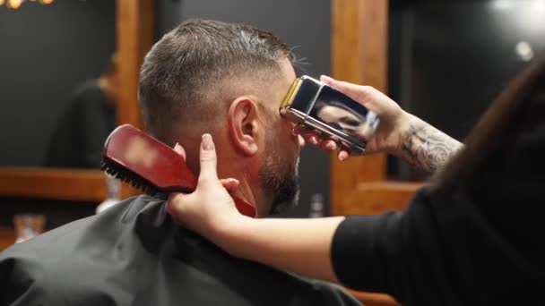 Attractive barber girl cutting mans hair with electric shaver. Female hair cutter working serving client. Stylish man sitting in vintage barber shop chair. Hairstylist woman doing trendy haircut. — Stock Video