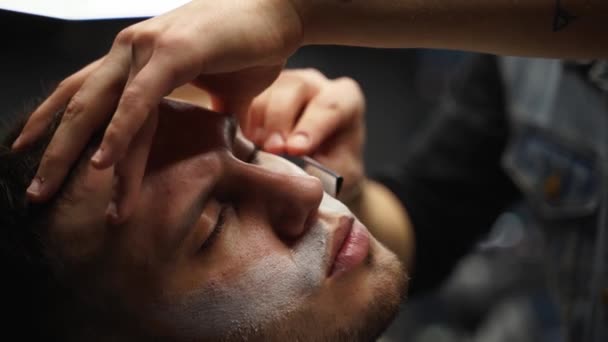 Barbeiro profissional barba barba do cliente com navalha reta. Barba cortada com lâmina antiquada na barbearia. Um macho bonito a rapar a barba no estúdio. Imagem de close-up . — Vídeo de Stock