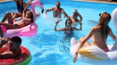 Arkadaşlar özel bir villada yüzme havuzunda parti yaparlar. Mayo giyen mutlu gençler su sıçratır, şamandıralarla dans eder ve güneşli bir günde lüks bir tatil köyünde şişme yatak giyerler. Yavaş çekim.