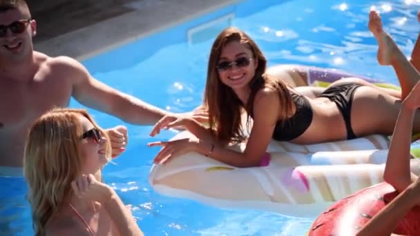 Amigos tienen fiesta en una piscina villa privada. Jóvenes felices en trajes de baño bailando, uniéndose y follando con flotadores y colchones inflables en un resort de lujo en un día soleado. Movimiento lento. — Vídeo de stock
