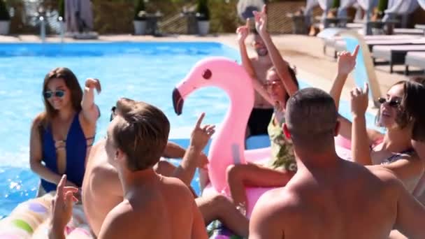 Des amis font la fête dans une villa privée piscine. Jeunes gens heureux en maillots de bain dansant, collant et clubbing avec des flotteurs et matelas gonflables dans un complexe de luxe par une journée ensoleillée. Mouvement lent. — Video