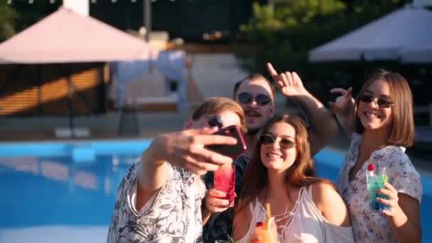 Amis souriants prenant selfie avec smartphone à la fête au bord de la piscine avec des cocktails colorés frais debout près de la piscine le jour ensoleillé d'été. Femme prenant des photos à la villa de luxe en vacances tropicales . — Video