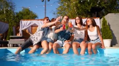 Bir grup arkadaş havuz başı partisinde bardakları tokuşturup taze kokteyllerle yüzme havuzunda dans ederek eğleniyorlar. İnsanlar tropikal tatillerde lüks villada içki içiyorlar. Slomo.