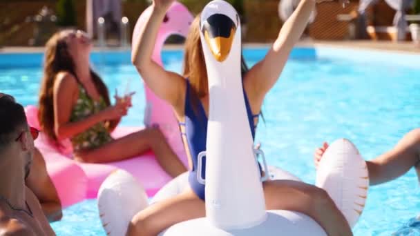 Vänner som har fest med cocktails i semestervilla pool. Glada unga människor i badkläder dans, klubbning med uppblåsbara flamingo, svan, madrass i lyx resort på solig dag. Långsamma rörelser — Stockvideo