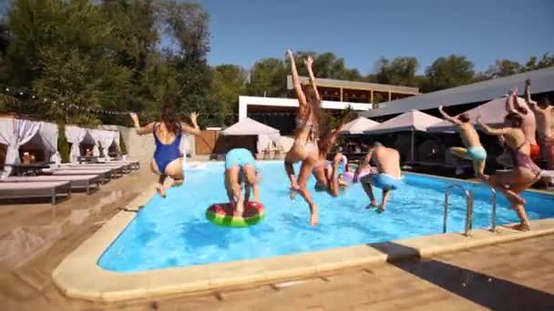 Gelukkige vrienden springen en spetteren in het zwembad met opblaasbare drijvers in luxe resort. Jongeren in zwemkleding hebben een feestje in een privé vakantievilla. Hete meisjes springen in het water op zomerdag. — Stockvideo