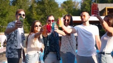 Bir grup arkadaş havuz başında yaz partisinde bardakları tokuşturup, yaz kokteyllerini yavaş çekimde yüzme havuzunda içiyorlar. İnsanlar taze meyve suyu içerek kadeh kaldırıyor. Tropikal tatilde lüks villa