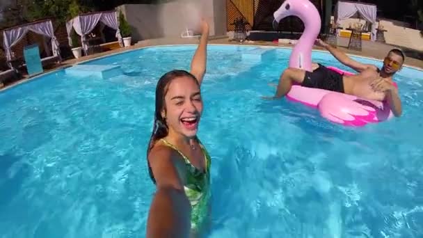 Estilo de vida blogger mujer tomando selfie video con cámara de acción en la piscina. Viajes vlogger films vlog de fiesta en un resort de lujo. Chica equipada en vivo streaming y relajarse con amigos de vacaciones — Vídeos de Stock