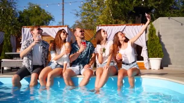 Amigos sorridentes tirando selfie com smartphone na festa na piscina com coquetéis coloridos frescos sentados à beira da piscina no dia ensolarado de verão. Mulher tirando foto na villa de luxo. Movimento lento . — Vídeo de Stock