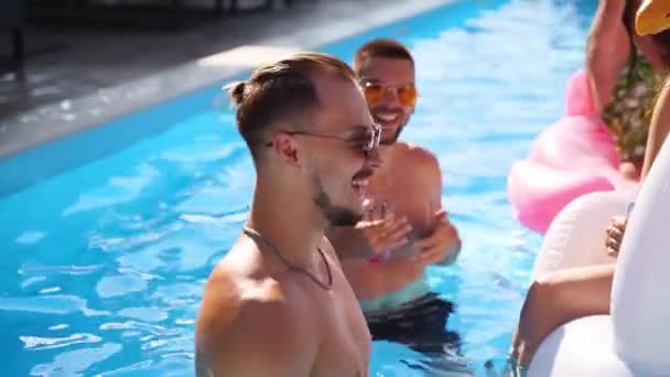 Vrienden die feesten met cocktails in het zwembad van de vakantievilla. Gelukkige jonge mensen in zwemkleding dansen, hechting, clubbing met opblaasbare flamingo, zwaan, matras in luxe resort op zonnige dag. — Stockvideo