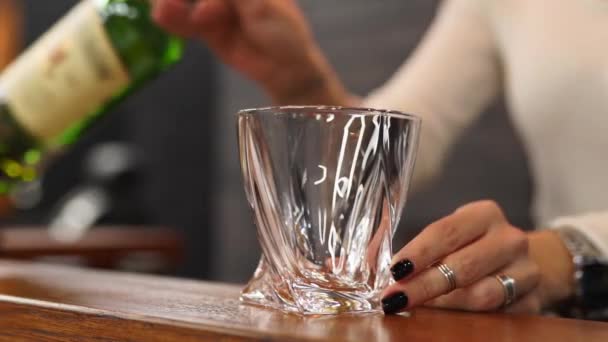 Deneyimli kadın şarap garsonu şişeden viski dolduruyor ve bardağı sallayarak alkol kokusu soluyor. Kadın eli, berber dükkanındaki ahşap tezgahta pahalı brendiyle cam taşıyor.. — Stok video