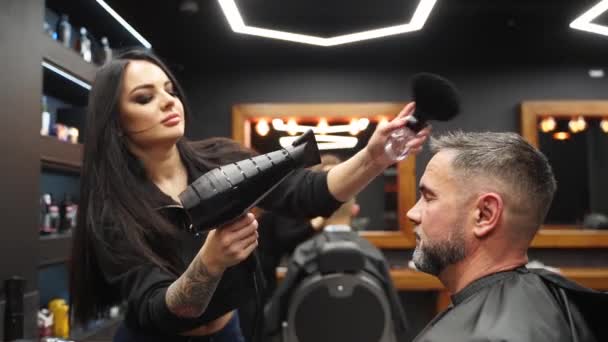 Wanita penata rambut bekerja dengan pengering rambut dan sikat di barbershop. Gadis tukang cukur bertato mengeringkan rambut pria setelah dipotong. Klien disajikan di studio rambut vintage. — Stok Video