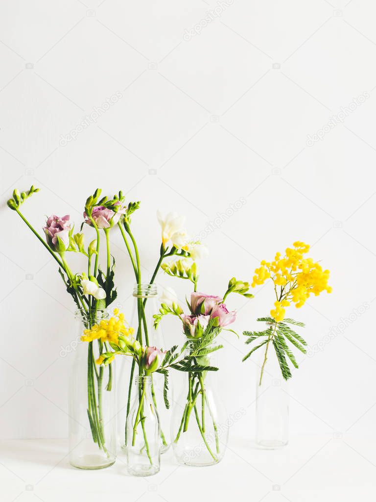 Still life of spring flowers in transparent bottles on a white t