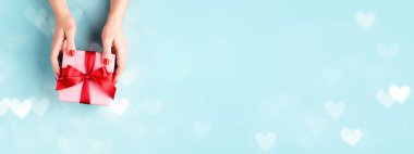 Mavi arka planda hediye kutusunu tutan kadın eller.