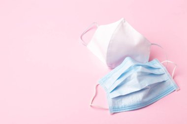 Mavi tıbbi maske ve pembe arka planda beyaz el yapımı yüz. Virüs kavramına karşı koruma.