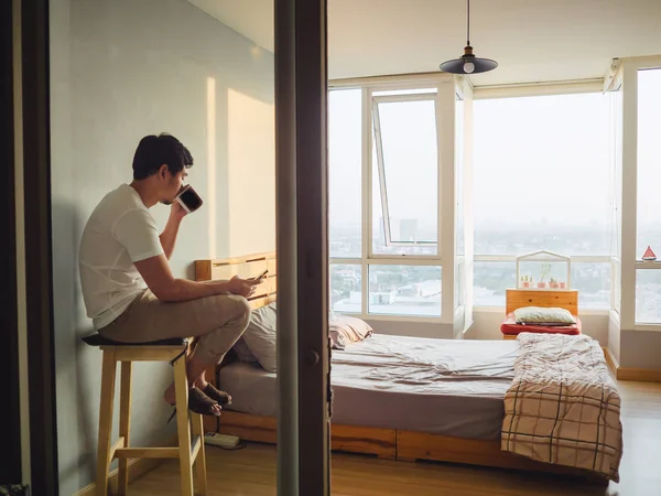 Одинокий человек болтает со смартфоном и пьет кофе в своей комнате — стоковое фото