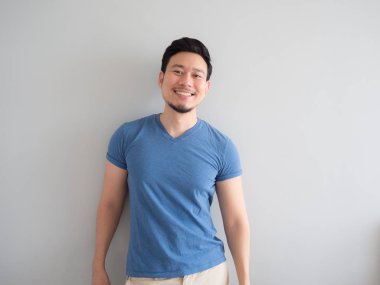 Gülümseme ve mavi t-shirt ve gri arka planda mutlu adam.