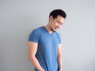 Gülümseme ve mavi t-shirt ve gri arka planda mutlu adam.