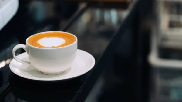 Gelas putih kopi latte panas di bar counter hitam . — Stok Foto