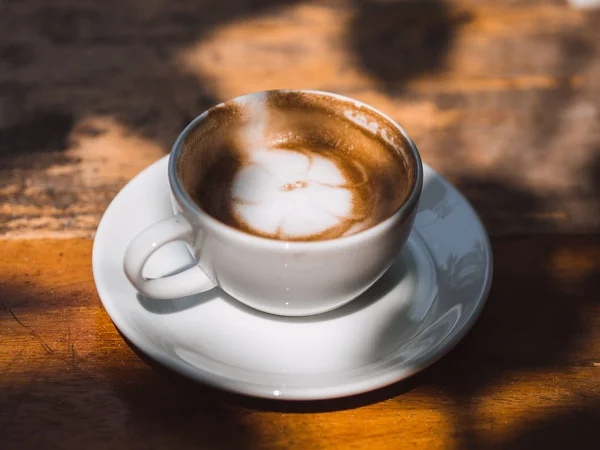 Wit warm kopje Latte koffie op houten tafel in de schaduw van de schaduw. — Stockfoto