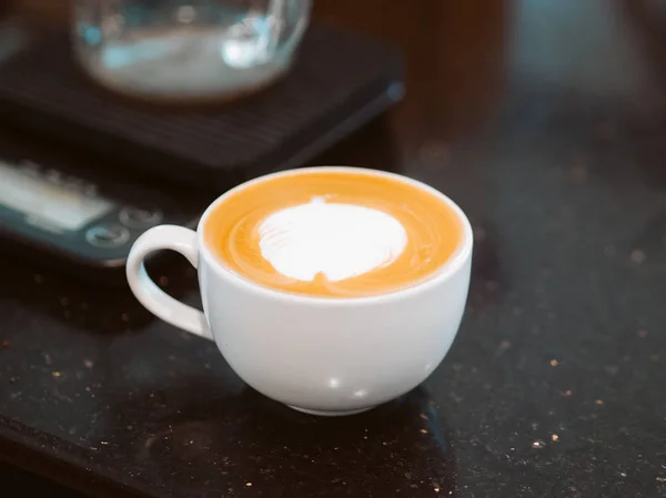 Gelas putih kopi latte panas di bar counter hitam . — Stok Foto