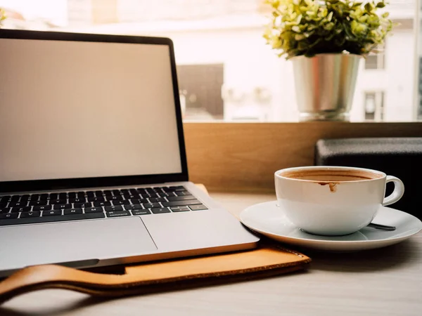Laptop und eine Tasse Kaffee mit Morgenlicht im Café. — Stockfoto