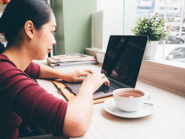 Kadın bir kafede sıcak kahve ile laptop kullanıyor.