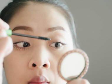Asyalı kadın onun kirpik makyaj maskara koyuyor.