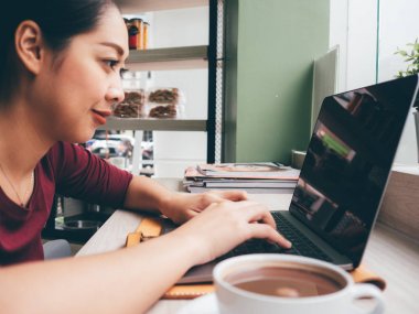 Asyalı kadın ile bir fincan sıcak kahve kafede dizüstü kullanıyor.