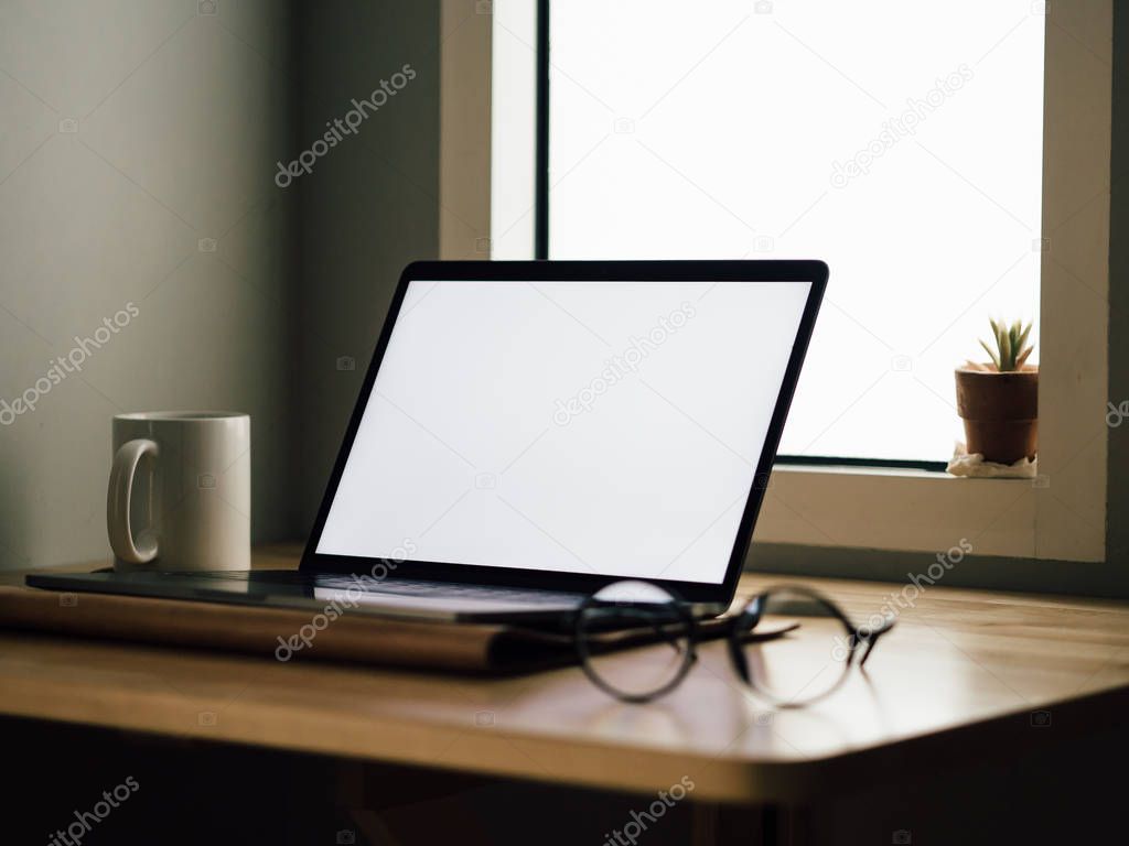 Laptop with white empty screen on wooden desk in the room of freelance office.