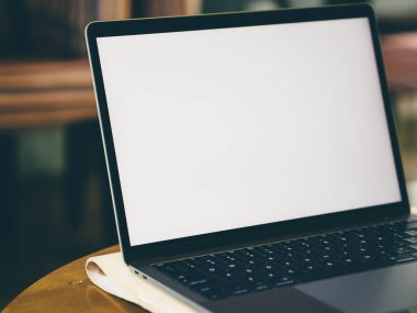 Kafedeki ahşap masa üstünde boş beyaz ekran laptop.