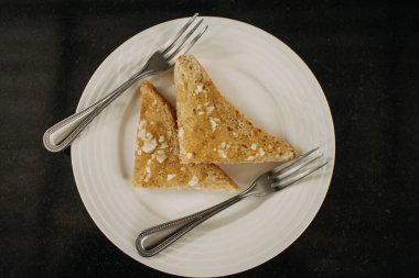 İki çatallı beyaz tabakta servis edilen sarımsaklı ekmek..