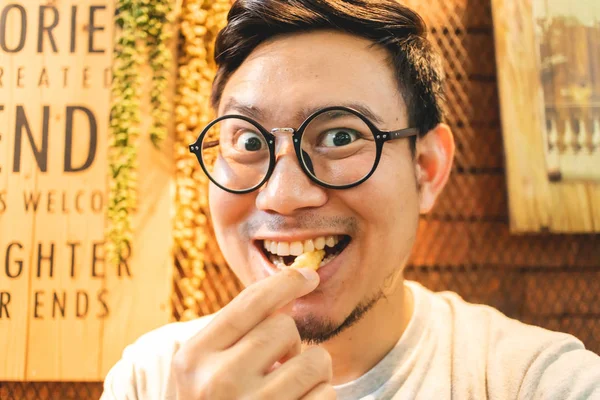 Funny delicious face of man eats French Fries in the cafe.