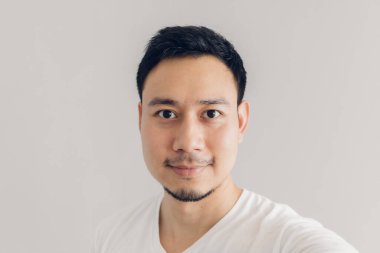 Smile Asyalı adam beyaz t-shirt ve gri arka plan ile kendini selfie alıyor.