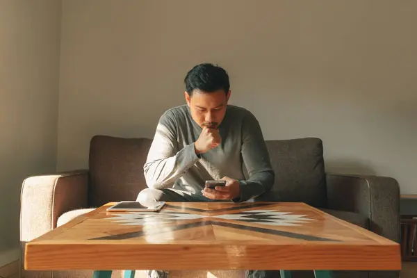 Asian man sits on the sofa in his living room, feeling relax in the morning.