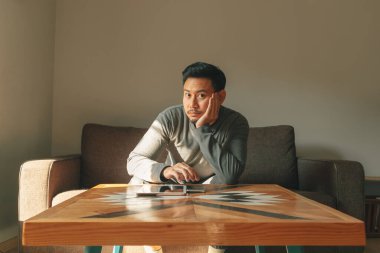 Asian man sits on the sofa in his living room, feeling relax in the morning.