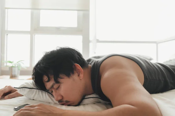 Sleepy man is using smartphone while lying on the bed. — Stock Photo, Image