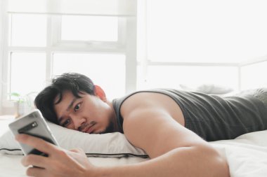 Uykulu adam yatakta yatarken akıllı telefon kullanıyor..