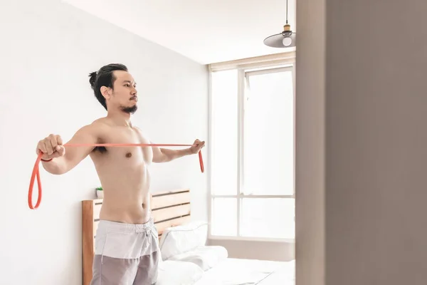 Hombre estirando su músculo en concepto de entrenamiento en casa con banda de resistencia . — Foto de Stock