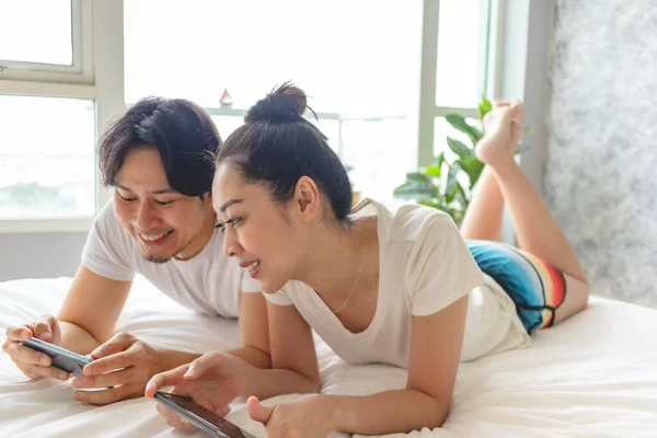Happy couple is playing mobile game together on their bed.