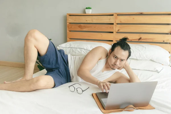 Homem está trabalhando de casa em roupas muito casuais e cabelo em sua cama . — Fotografia de Stock