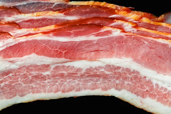Bacon fresco com carne e gordura em um fundo preto close-up — Fotografia de Stock