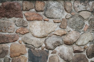 Taş bir duvarın arka planı, yakın plan. Betondaki büyük ve küçük renkli taşların dokusu. Birçok taştan yapılmış eski sert beton duvar.