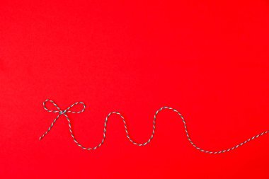 Kırmızı arka planda üç renkli festival kurdelesinden yapılmış el yapımı yay. Minimalizm. Boşluğu kopyala.