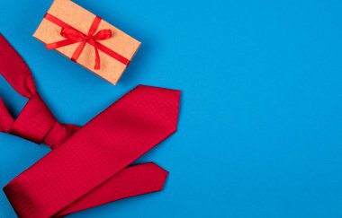 Greeting card with composition of red neck tie and gift box with bow on blue cyan background.