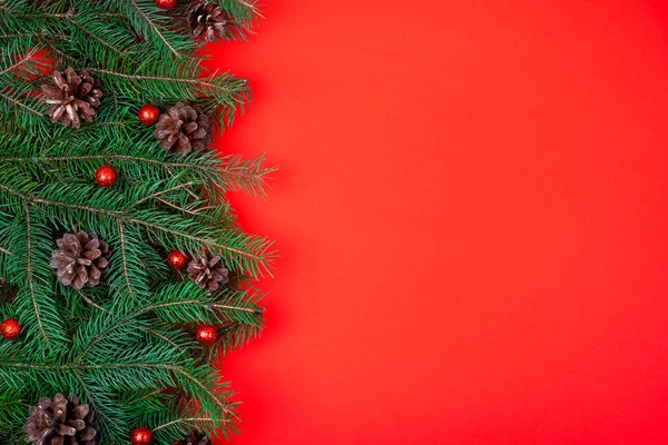 赤いお祝いの背景に松のコーンで飾られたクリスマスツリーの枝。平敷. — ストック写真